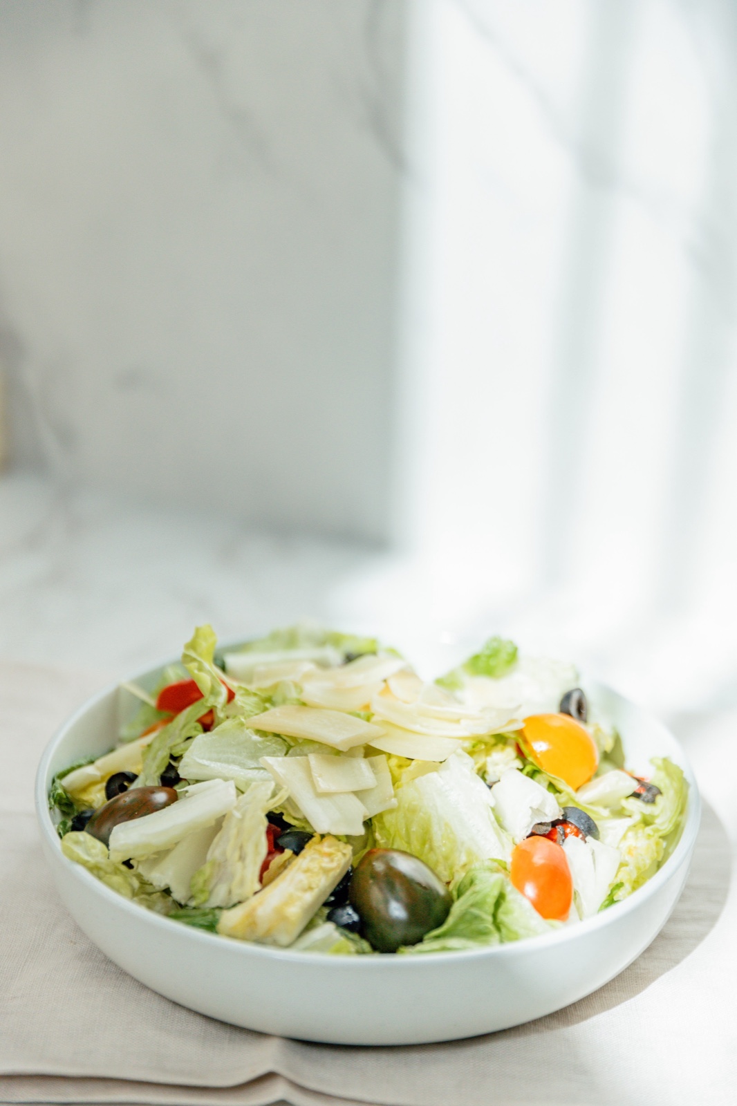 Italian salad in a white bowl with shaved parmesan, olives, tomatoes, and onion